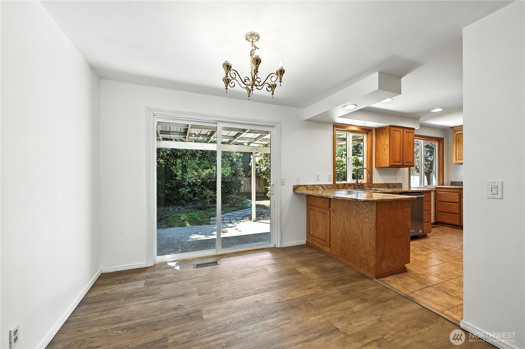 Vacant kitchen with warm wood cabinets and granite peninsula beside a sliding door to the garden.
