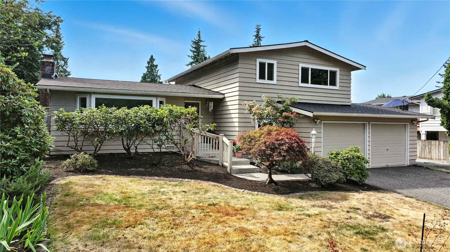 Beige split-level home with a two-car garage, front garden, and dry lawn.