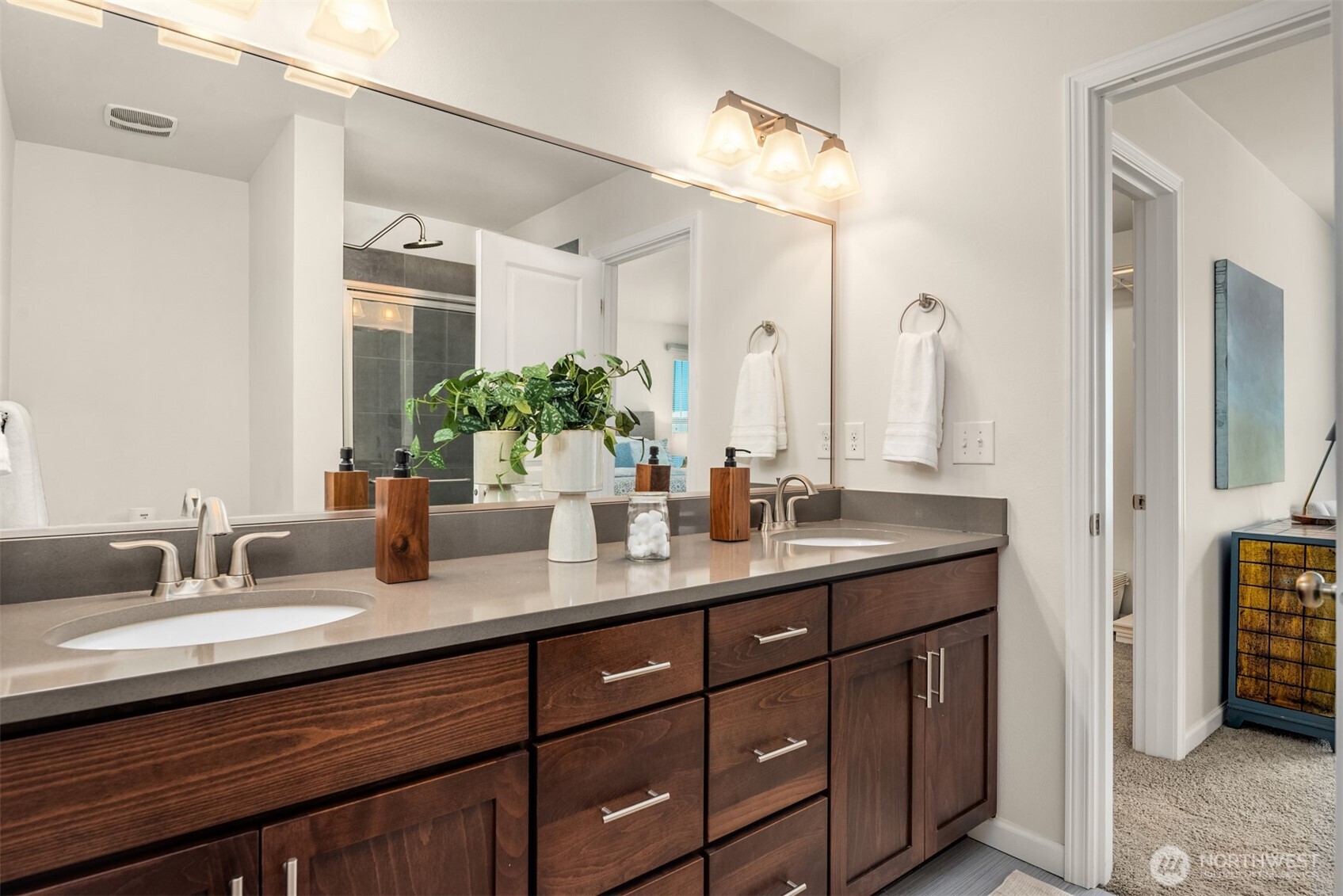 Bathroom vanity with two sinks, dark wood cabinetry, a large mirror, and a potted plant.
