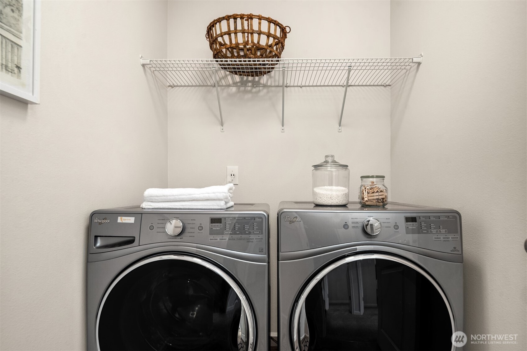 Laundry room with matching front-loading washer and dryer beneath a wire shelf.