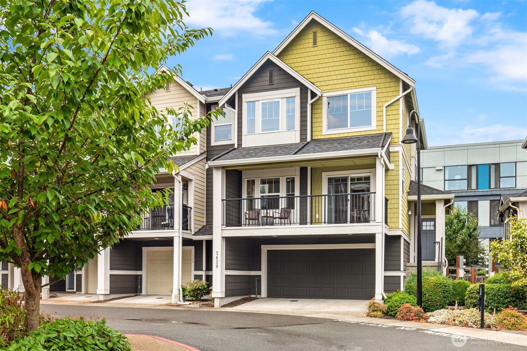 Multistory townhouse with yellow siding, a two-car garage, and a covered balcony.
