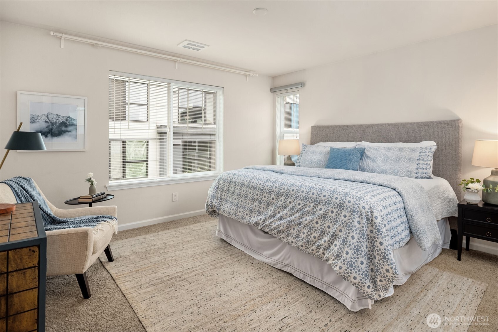 Staged bedroom with blue-and-white bedding, a gray headboard, and wide windows with blinds.