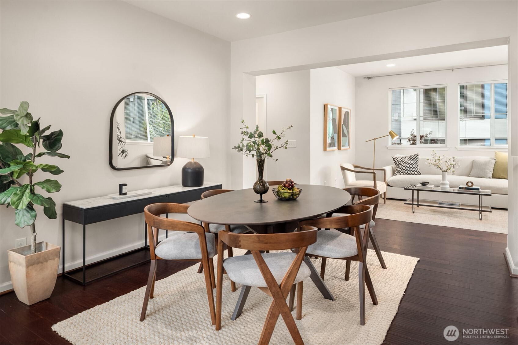 Dining area with a round wooden table and chairs opening onto a bright living room.