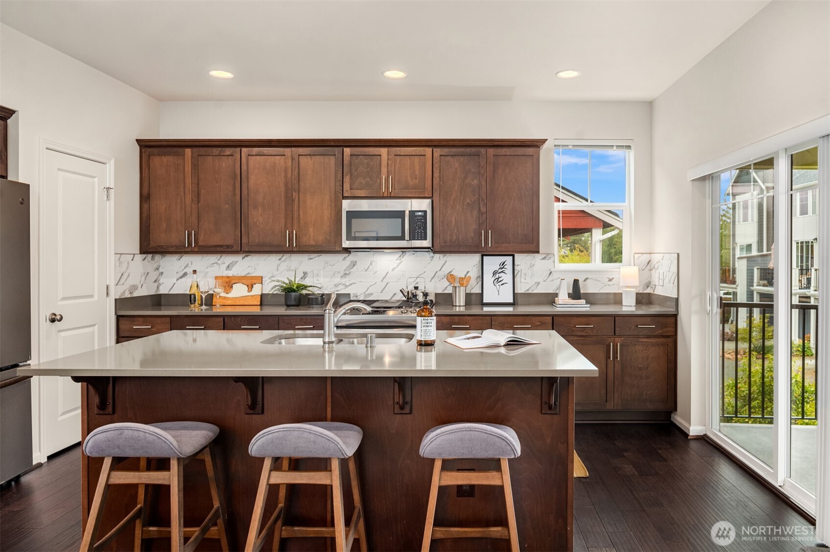Kitchen with dark wood cabinets, a large island, three stools, and sliding doors to a balcony.