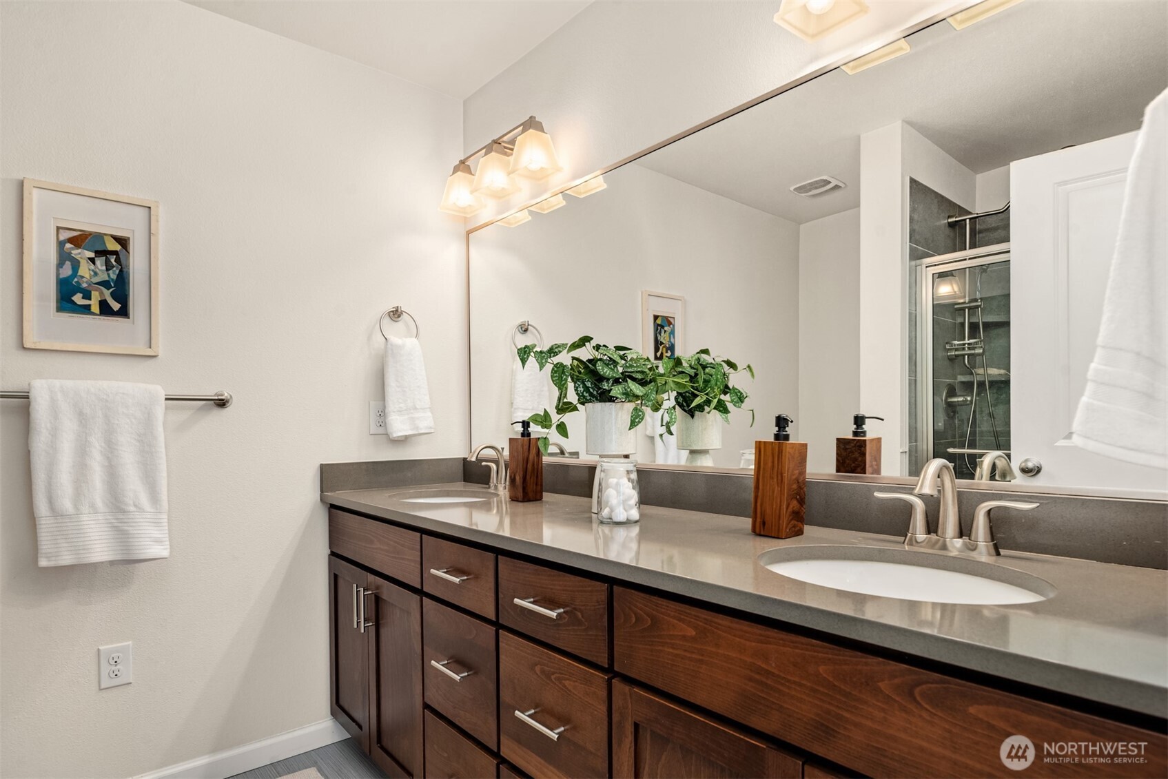Bathroom with a long dark wood double-sink vanity and a glass-enclosed dark-tile shower.