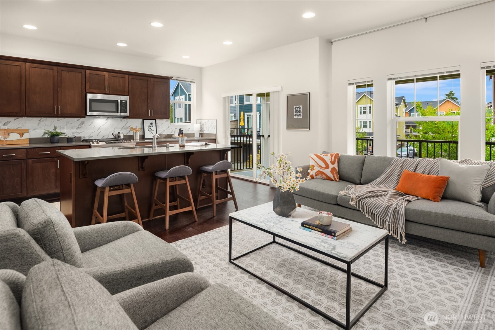 Open living room and kitchen with a marble island, dark wood cabinets, gray sofas, and large windows.