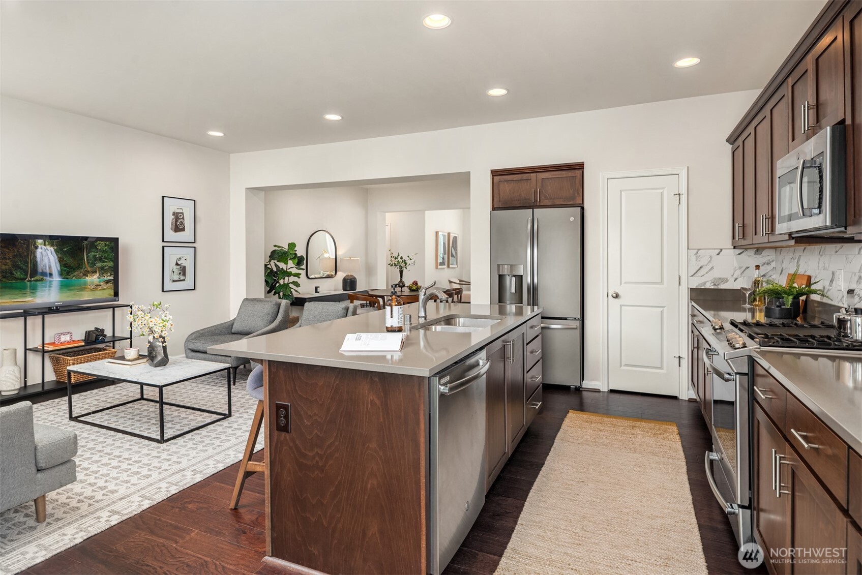Open-plan kitchen with a large island, dark wood cabinets, stainless steel appliances, and adjoining living area.