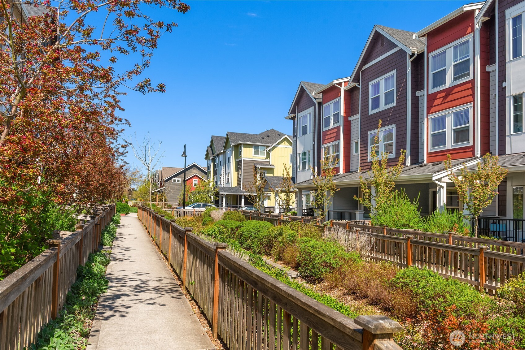 Colorful townhomes line a landscaped walkway with wooden railings and autumn trees.