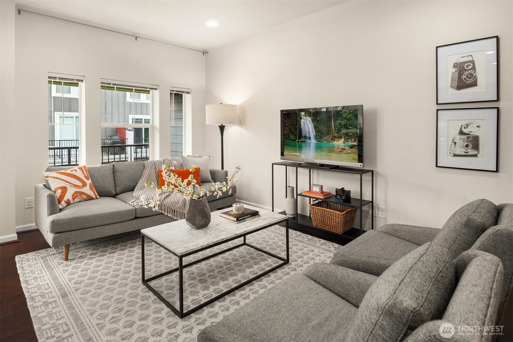 Staged living room with gray sofas, marble-top coffee table, patterned rug, and tall windows.