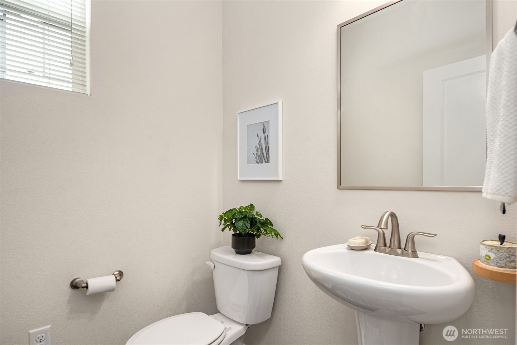 Bright bathroom with a pedestal sink, large mirror, and potted plant beside the toilet.