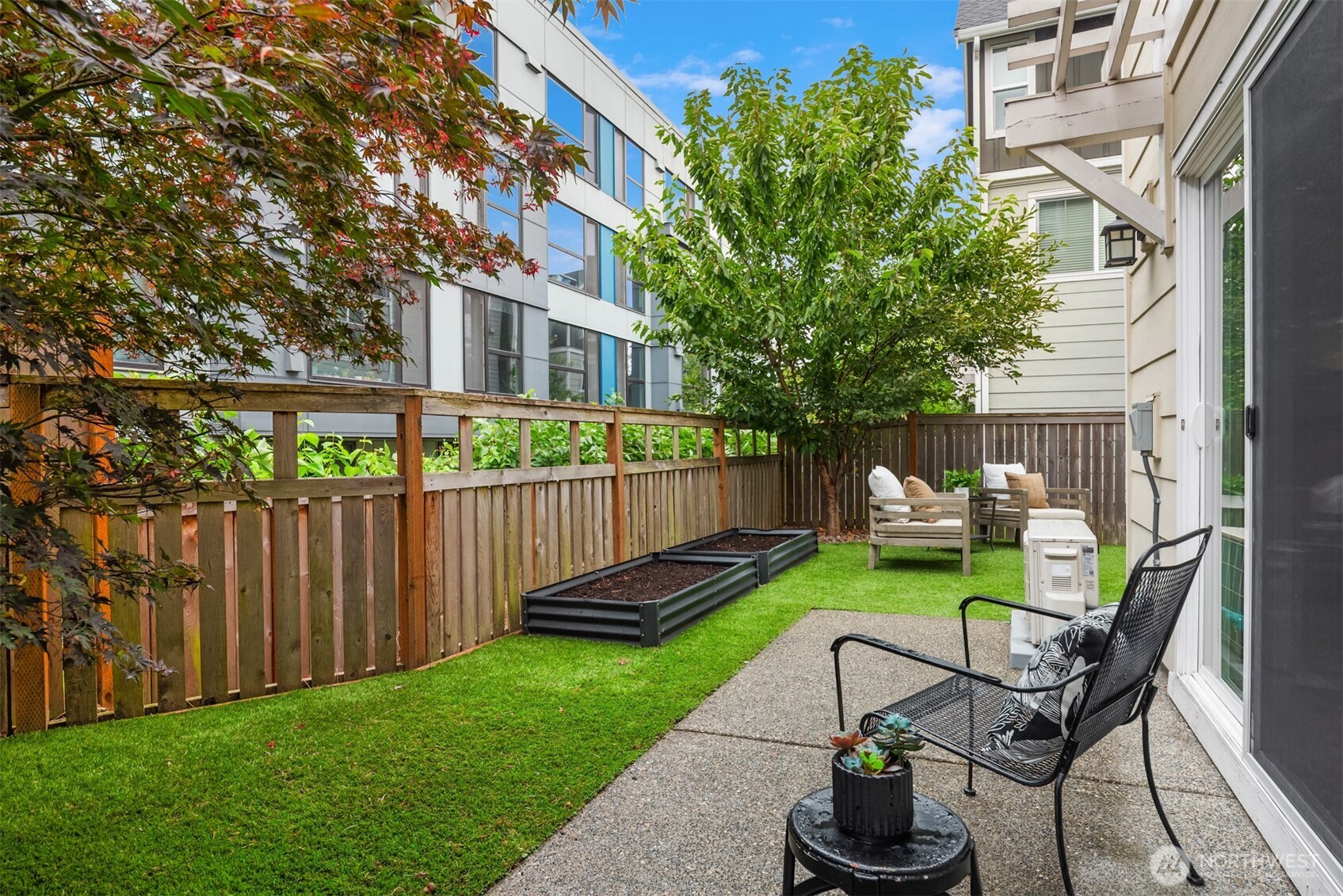 Private townhouse patio with fenced lawn, raised garden beds, and outdoor seating.