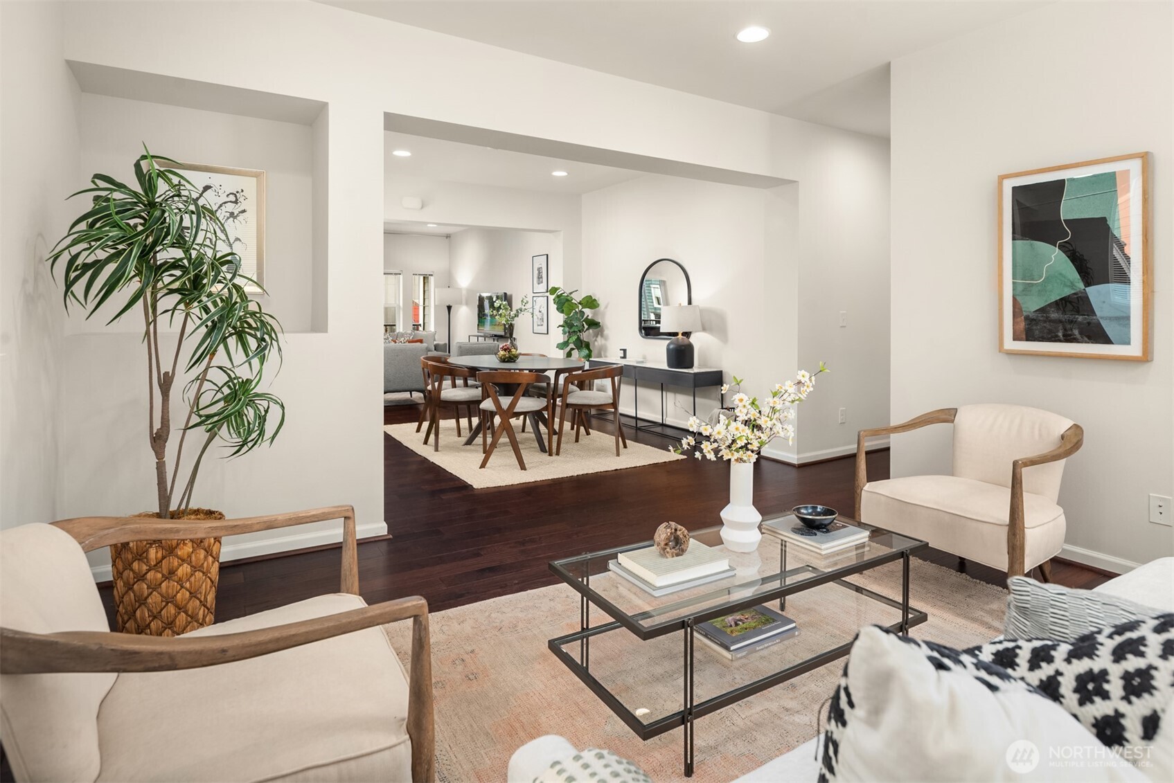 Staged living room opening into a dining area, with dark hardwood floors and a glass coffee table.