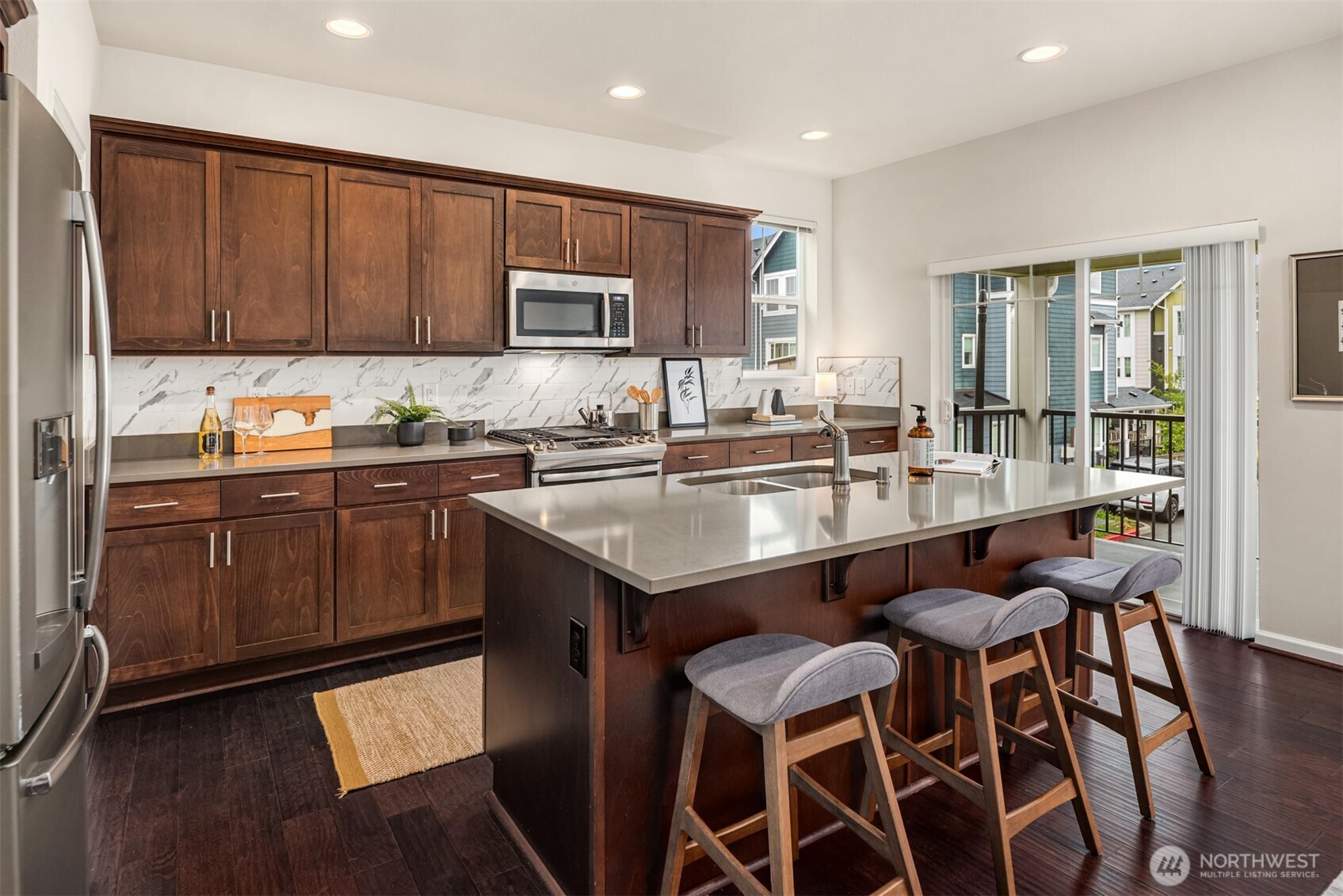 Kitchen with dark wood cabinets, stainless appliances, and a large island with bar stools.
