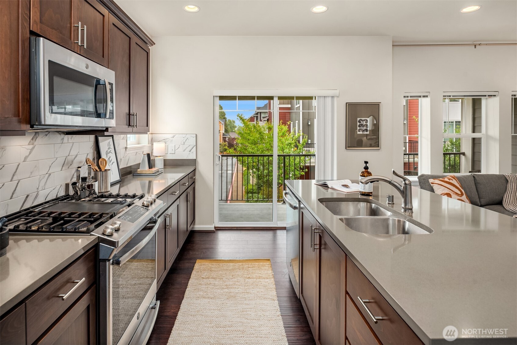 Condo kitchen with dark wood cabinets, stainless appliances, and an island facing a balcony.