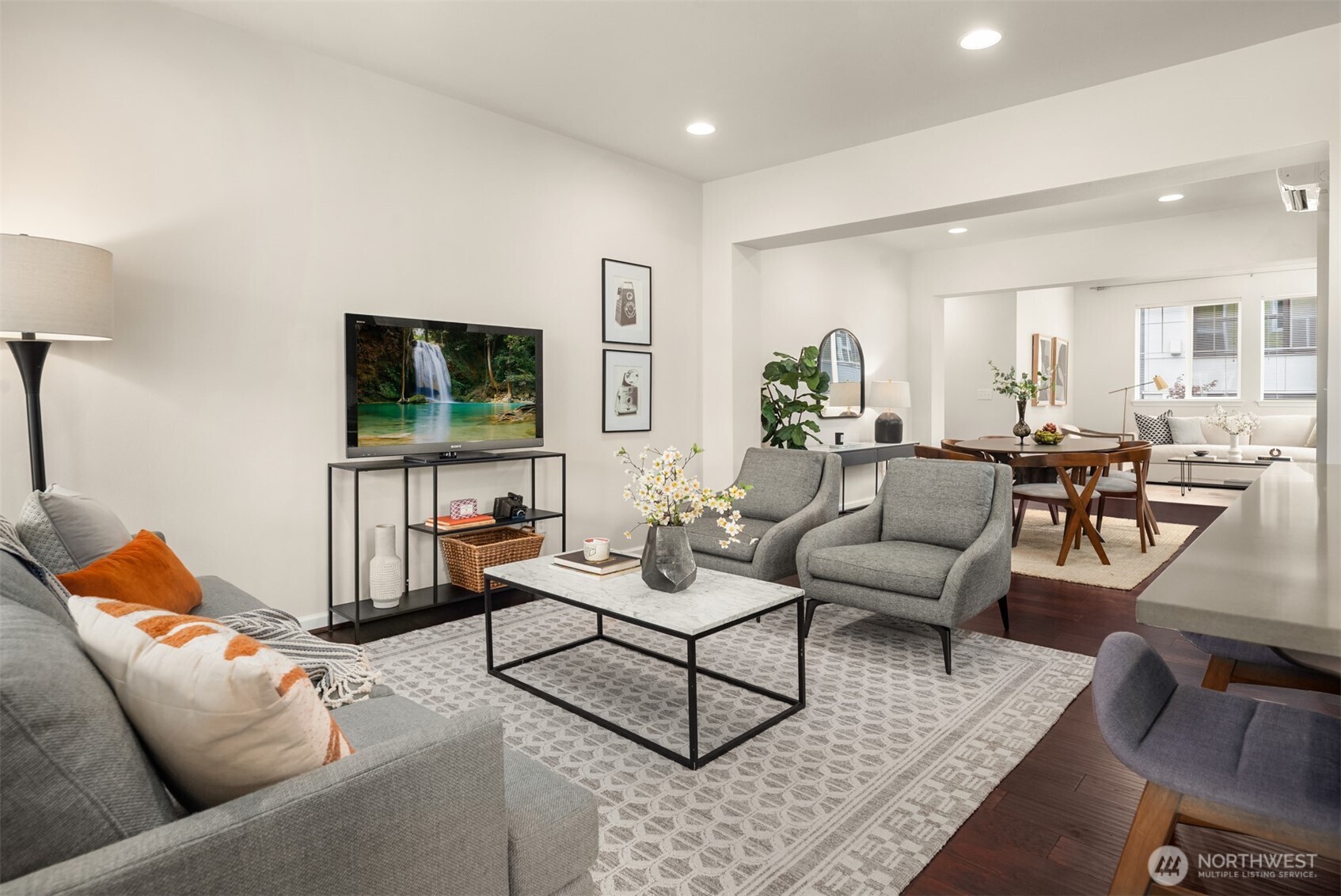 Staged living room with gray seating, marble coffee table, and adjoining dining area.