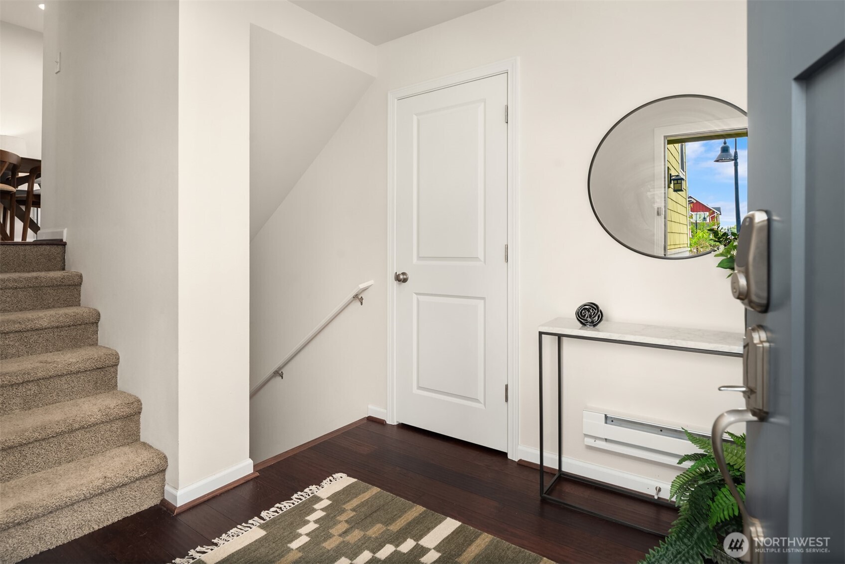 Entry foyer with carpeted stairs, dark hardwood floors, round mirror, and marble-top console table.