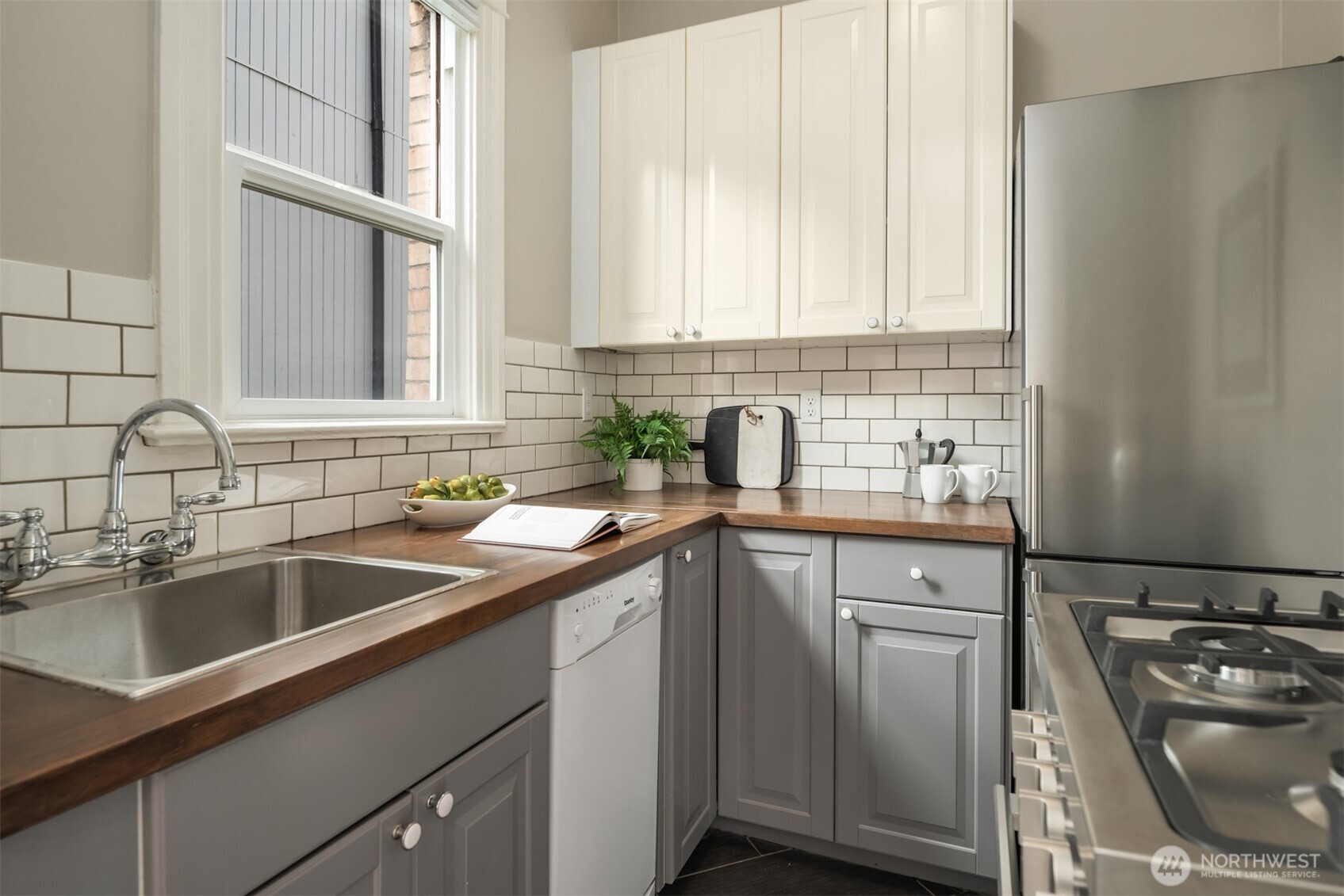Kitchen with dark wood counters, gray cabinets, subway-tile backsplash, and a window above the sink.