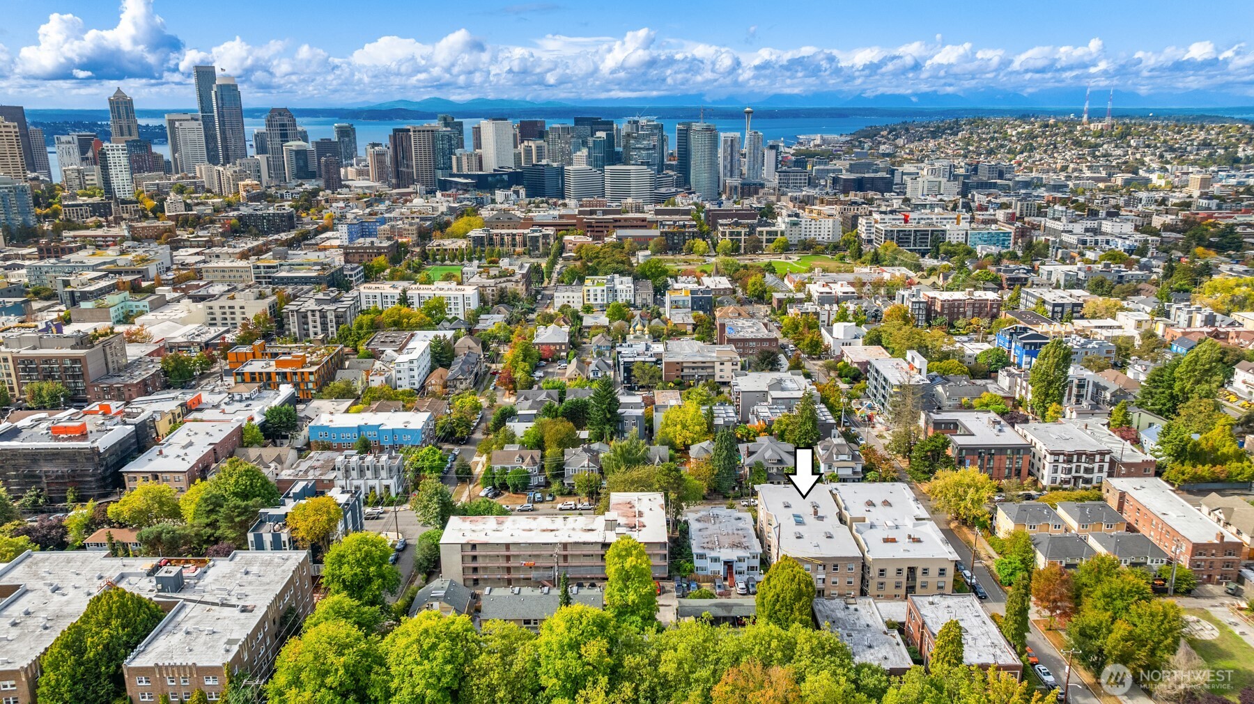 Aerial Seattle view toward downtown, Elliott Bay, and mountains, with an arrow marking the apartment building.
