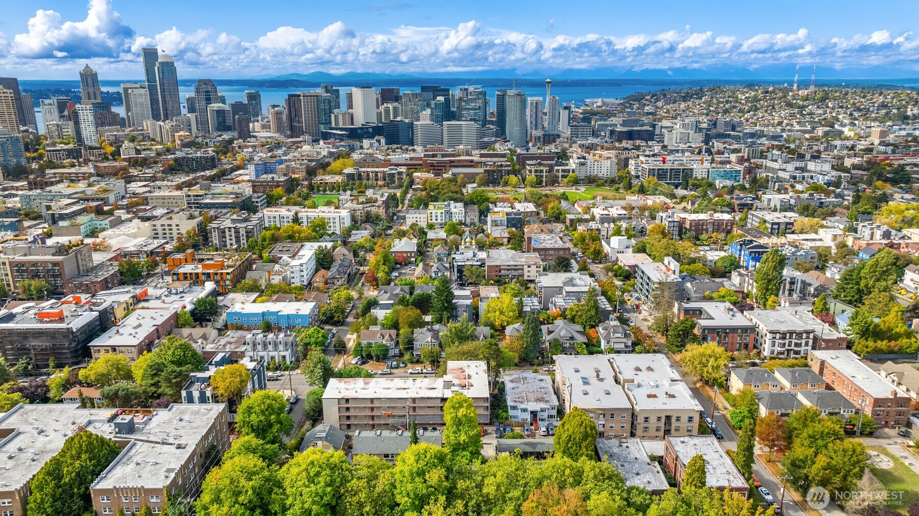Aerial view of Seattle with the downtown skyline, Space Needle, Puget Sound, and mountains beyond.