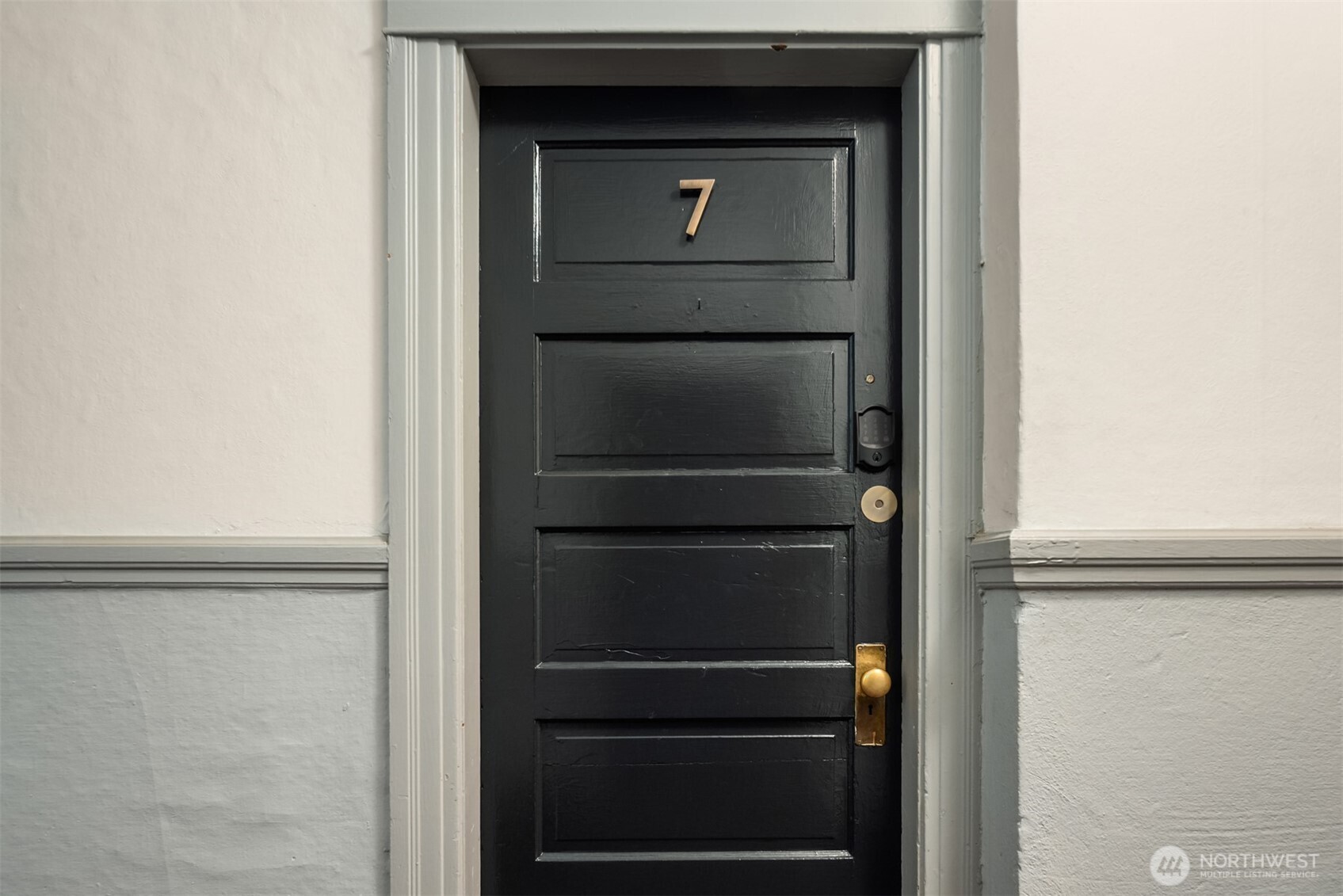 Dark paneled unit door numbered 7 with brass hardware and a keypad lock.