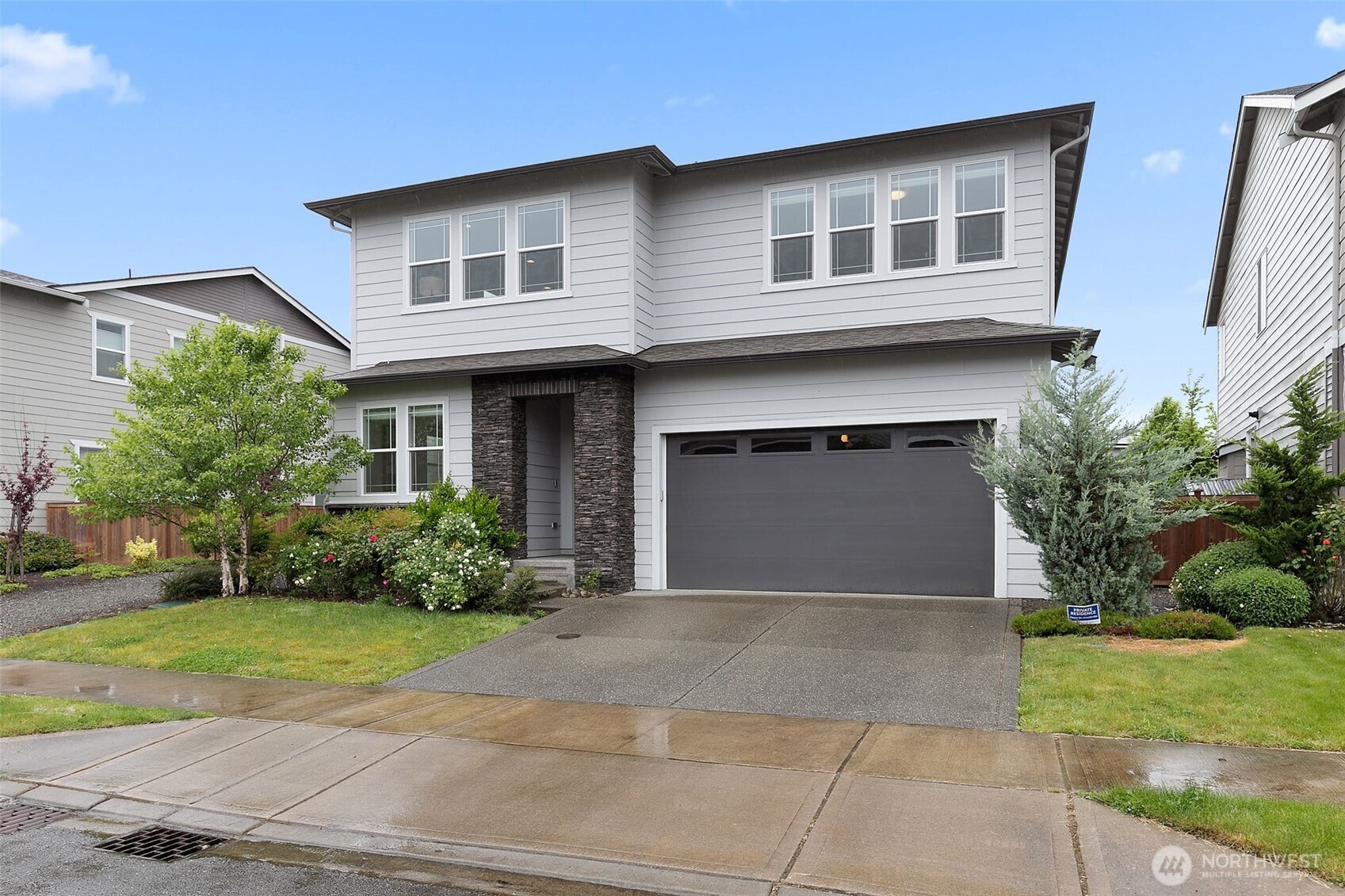 Two-story gray home with stone entry columns, a wide garage, and landscaped front yard.