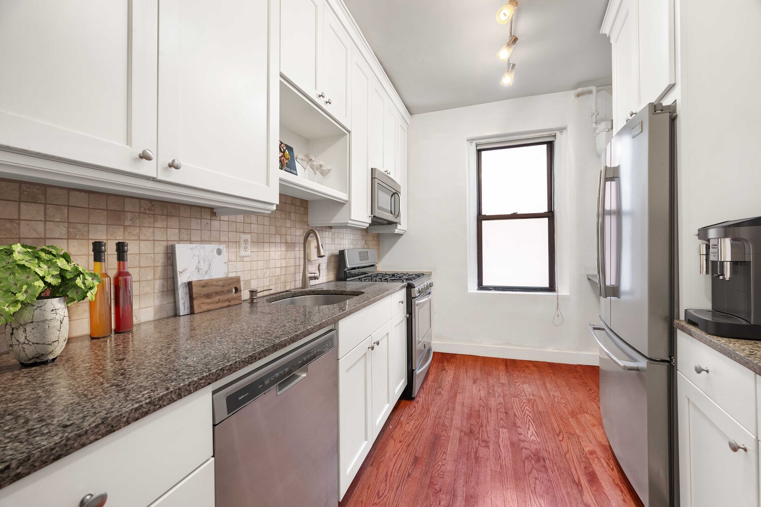 Galley kitchen with white cabinets, granite counters, stainless steel appliances, and hardwood floors.