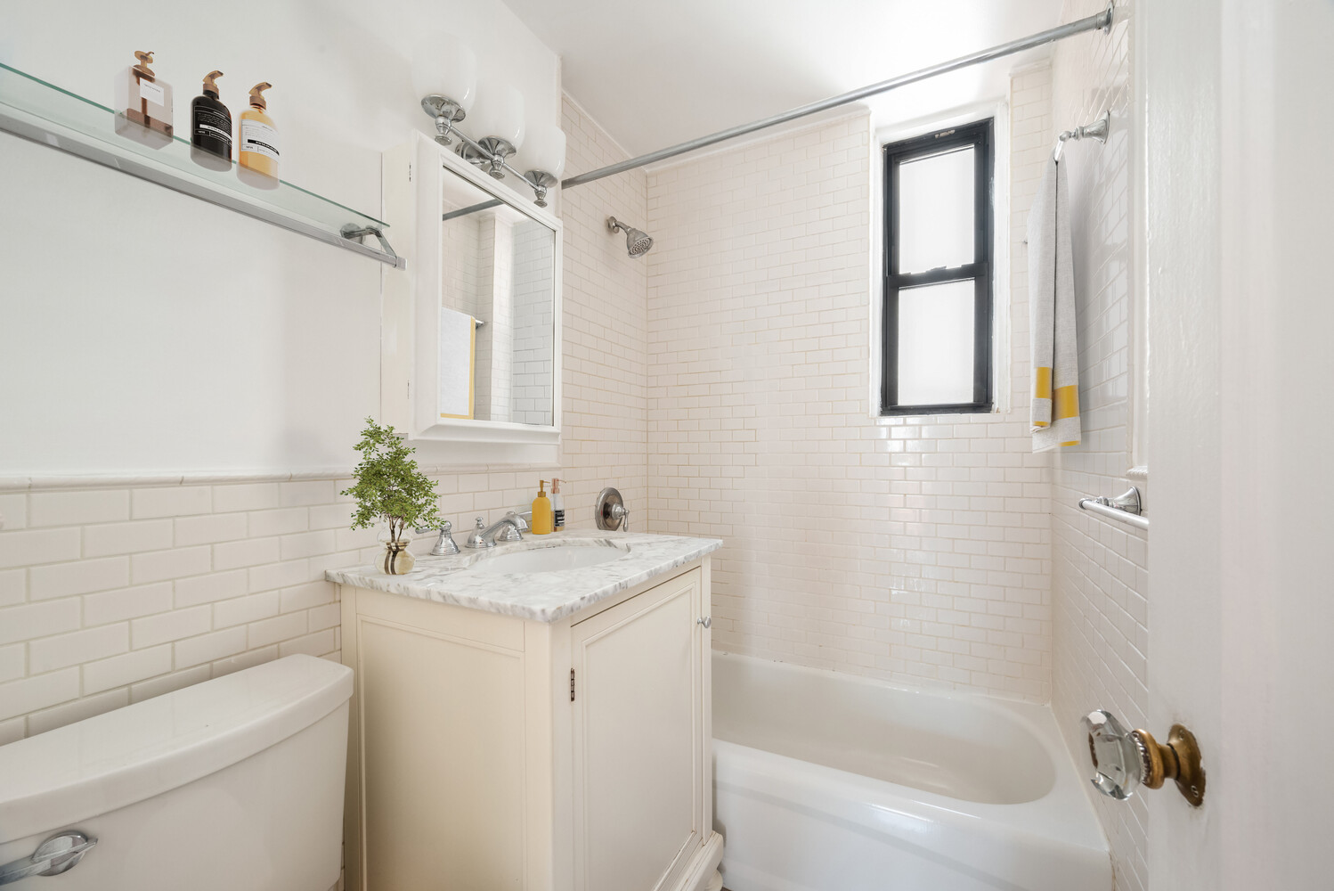 Bathroom with white subway tile, a marble-topped vanity, and a bathtub beneath a black-framed window.
