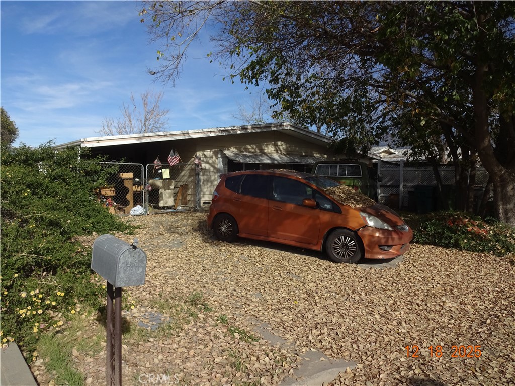 Single-story house behind a chain-link fence, with an orange car in the leaf-covered driveway.