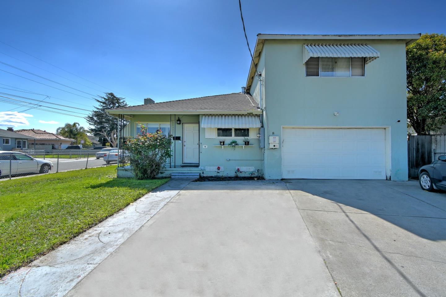 Pale blue house with a large white garage door, striped awnings, and a wide concrete driveway.
