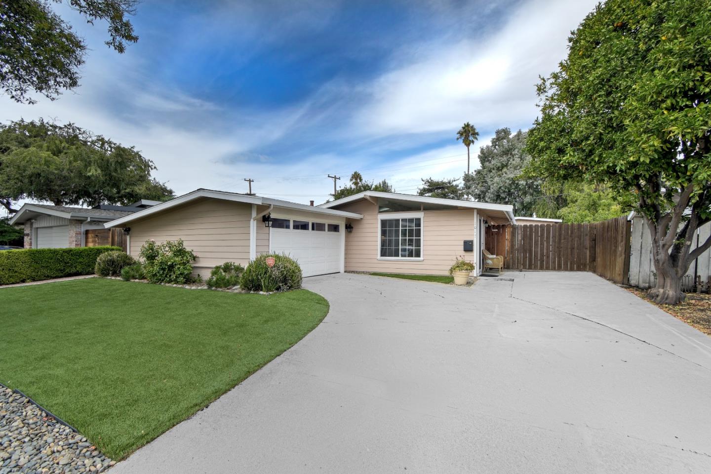Single-story beige home with a white garage door, curved lawn, and broad concrete driveway.
