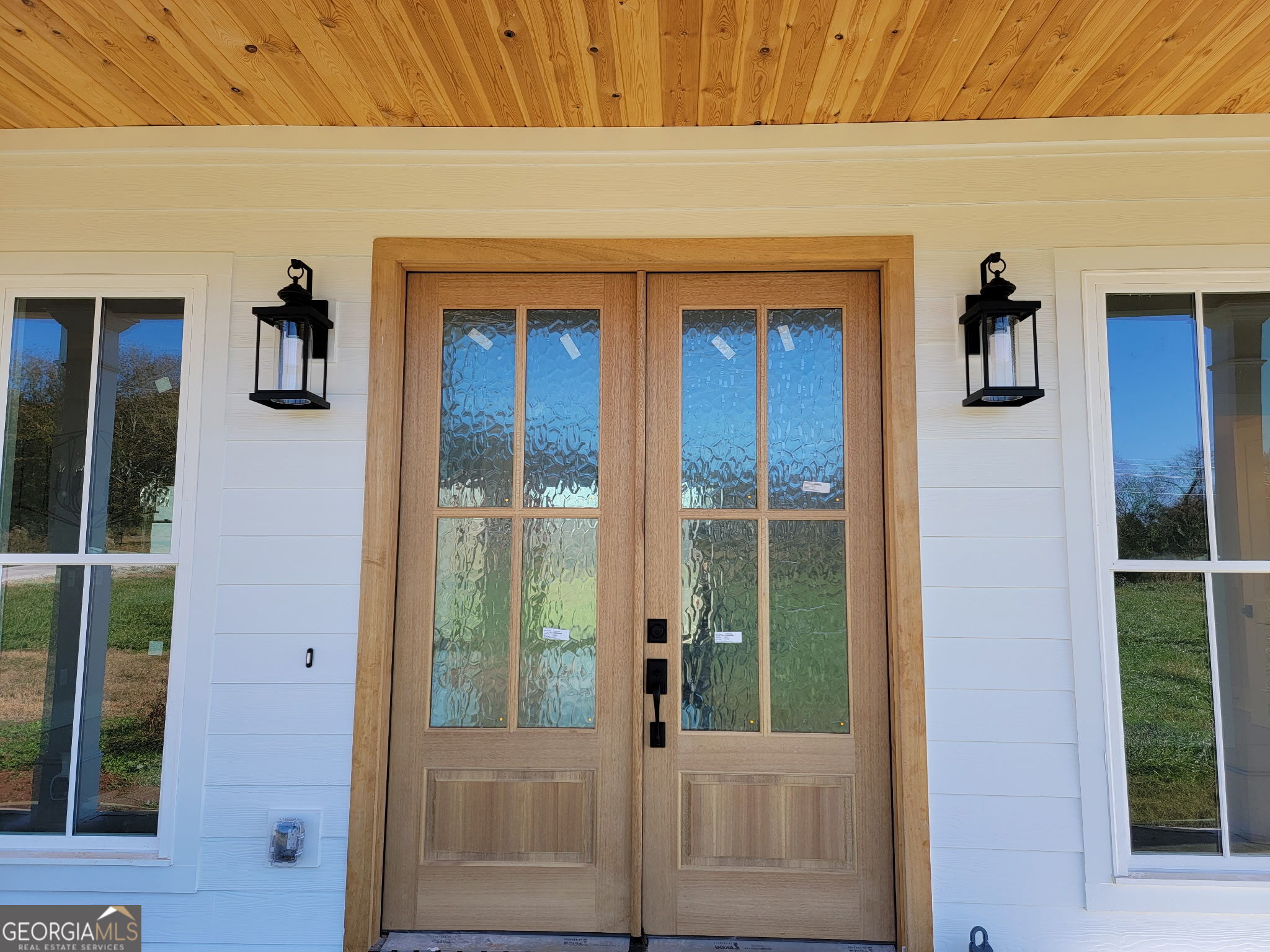 Wooden double front doors with textured glass, flanked by black lanterns and windows.