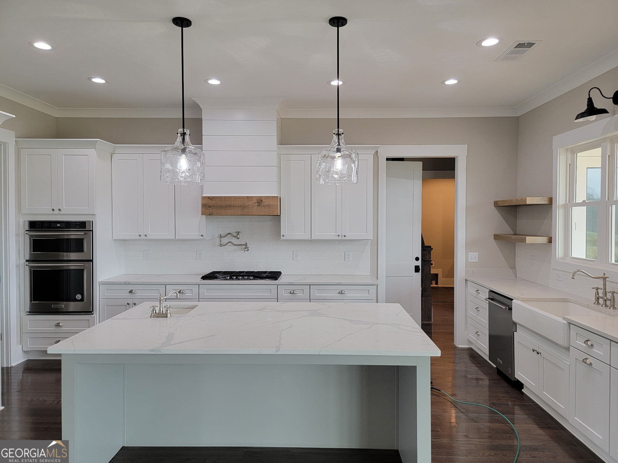Bright white kitchen with a large marble-look island, farmhouse sink, and double wall ovens.