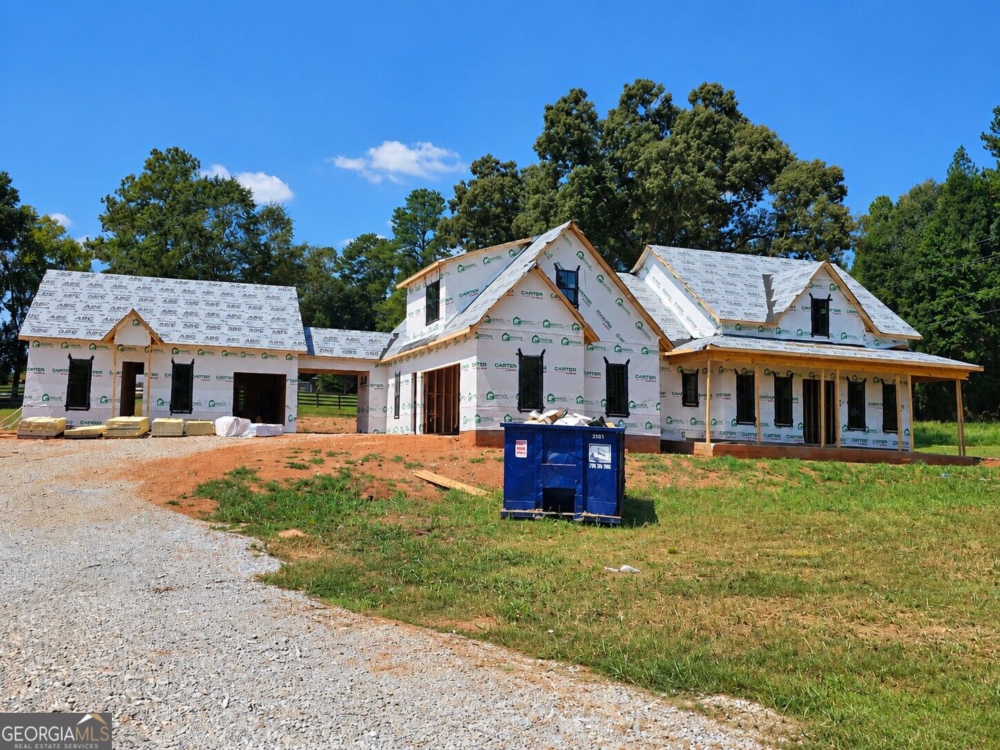 Two-story house under construction with multiple gables and a blue dumpster in front.