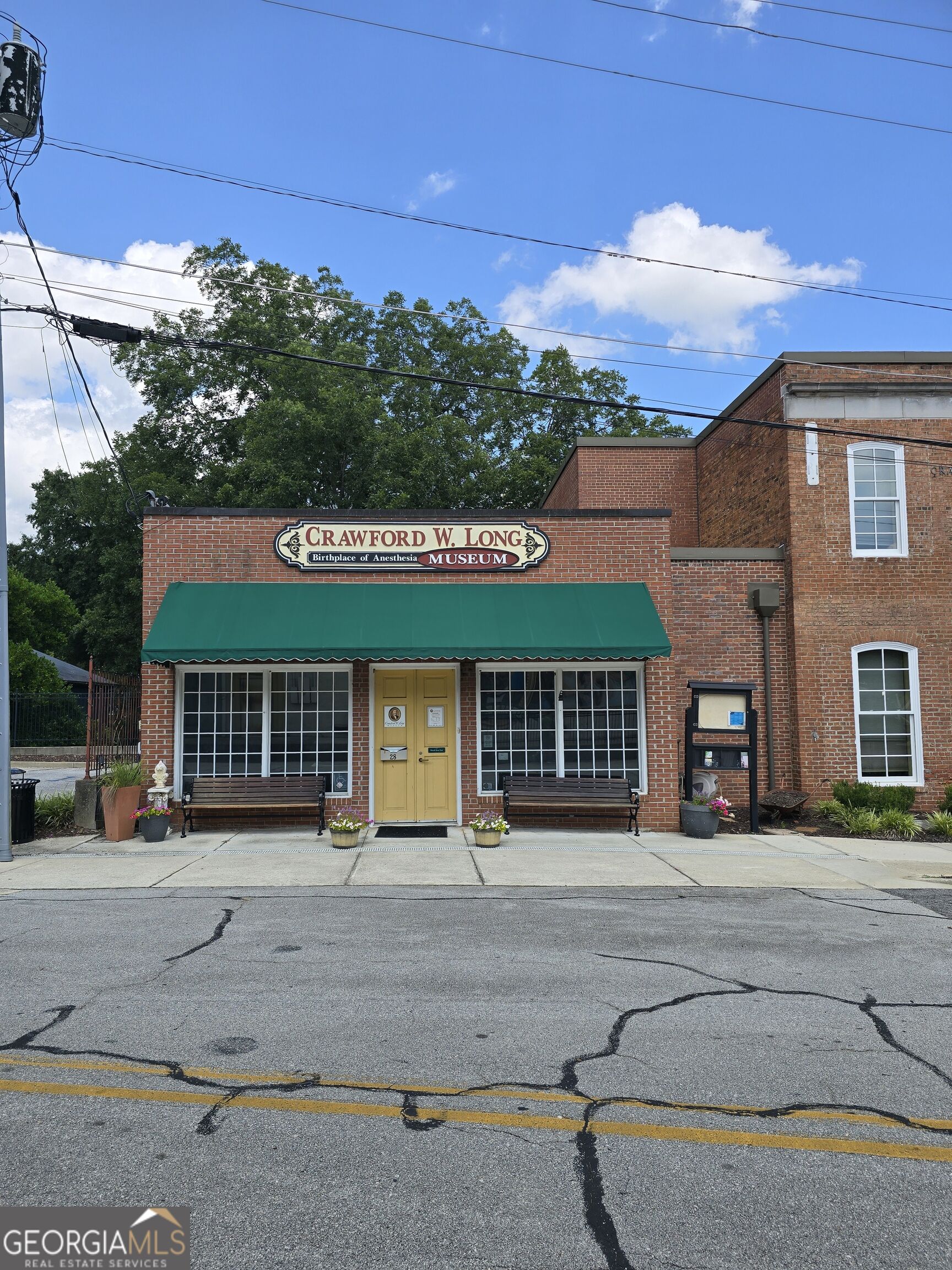 Brick museum facade with a green awning, yellow entrance door, and Crawford W. Long Museum sign.