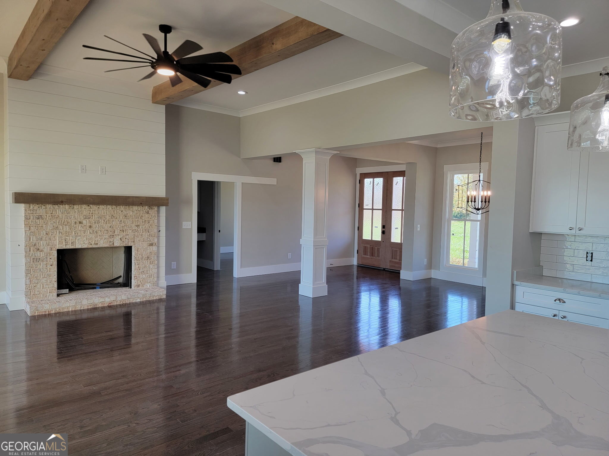 Open-plan living room with a stone fireplace, exposed ceiling beams, and dark hardwood floors.