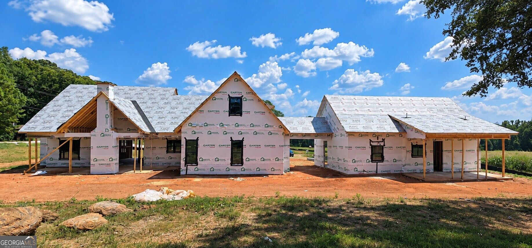 Large home under construction with multiple gabled roof sections on a cleared rural lot.