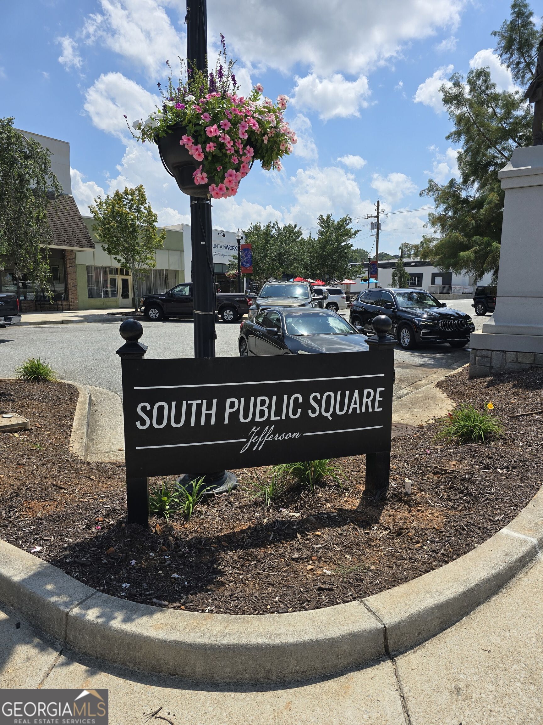 South Public Square sign in Jefferson, with a hanging basket of pink flowers and downtown storefronts.
