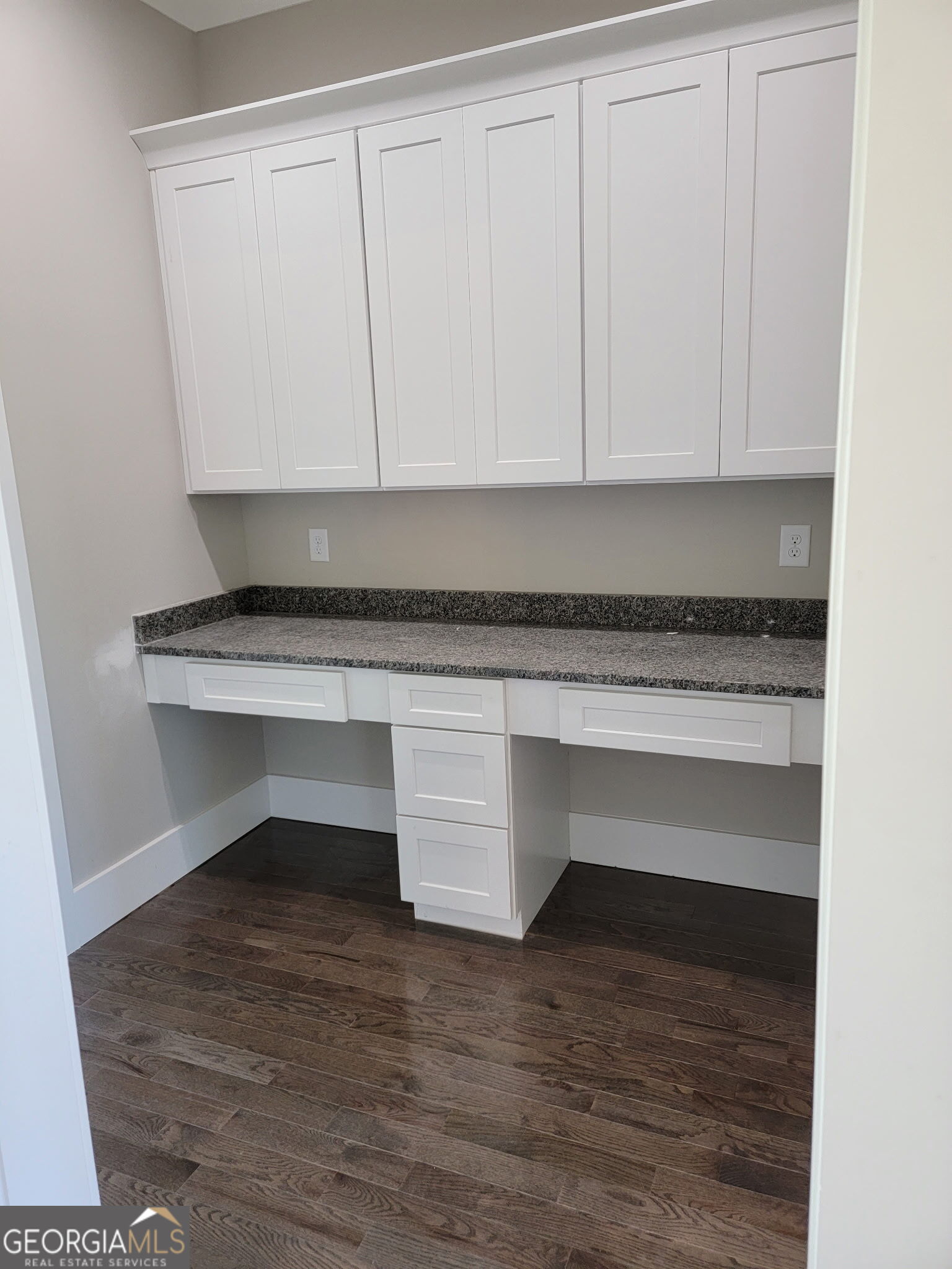 Built-in office nook with white cabinets, a dark speckled countertop, and wood flooring.