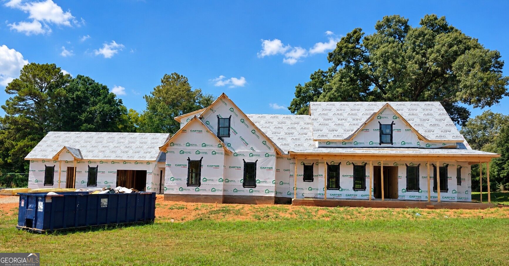 Large two-story home under construction with multiple gables and a blue dumpster in front.