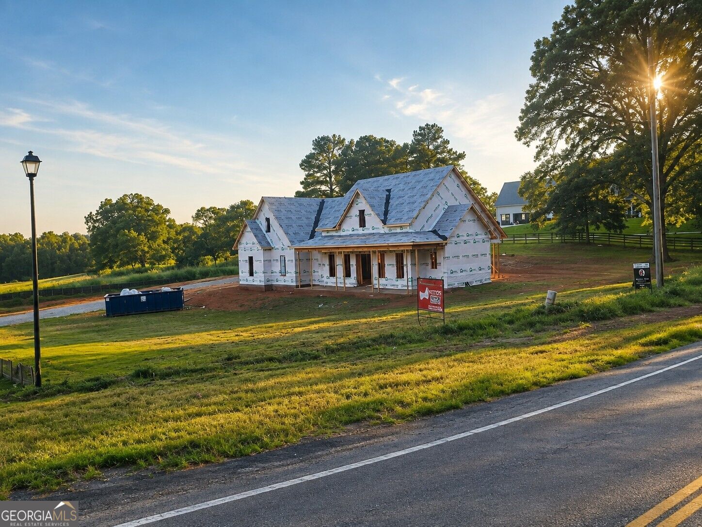 House under construction on a grassy lot beside a road at sunset.