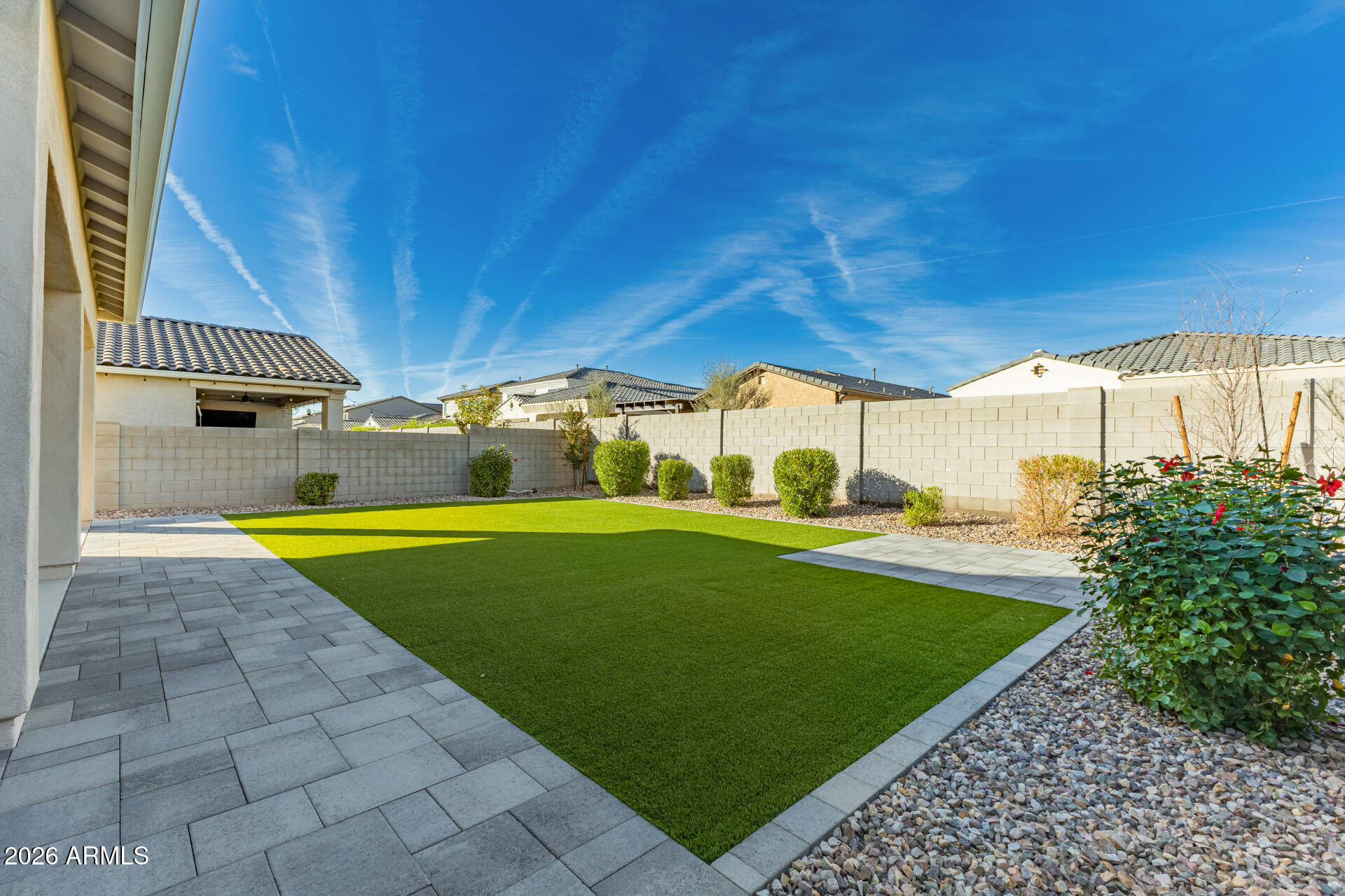 Backyard with artificial turf, gray paver patio paths, and a block wall.
