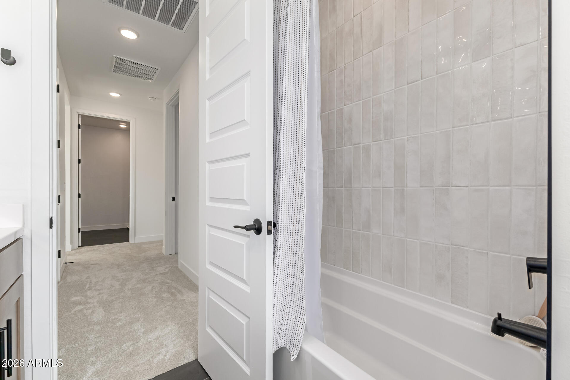 Bathroom with a tiled tub and black fixtures opening onto a carpeted hallway.