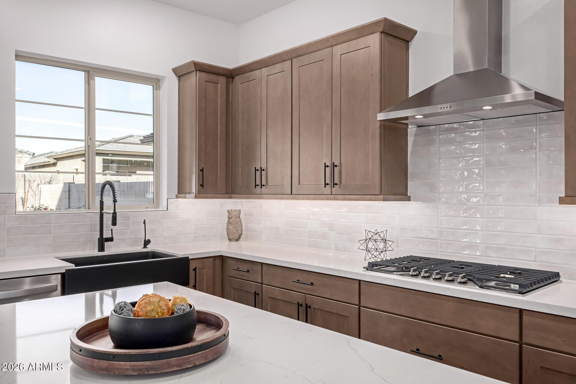 Kitchen with warm wood cabinets, white tile backsplash, black farmhouse sink, and stainless-steel range hood.
