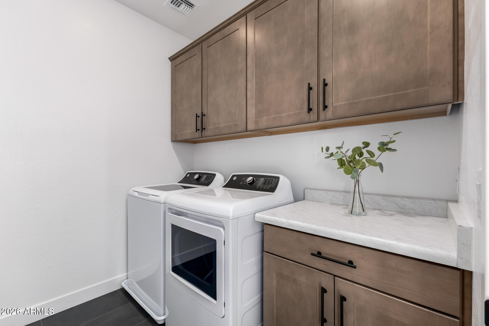 Laundry room with washer and dryer, taupe cabinets, and a marble-look countertop.