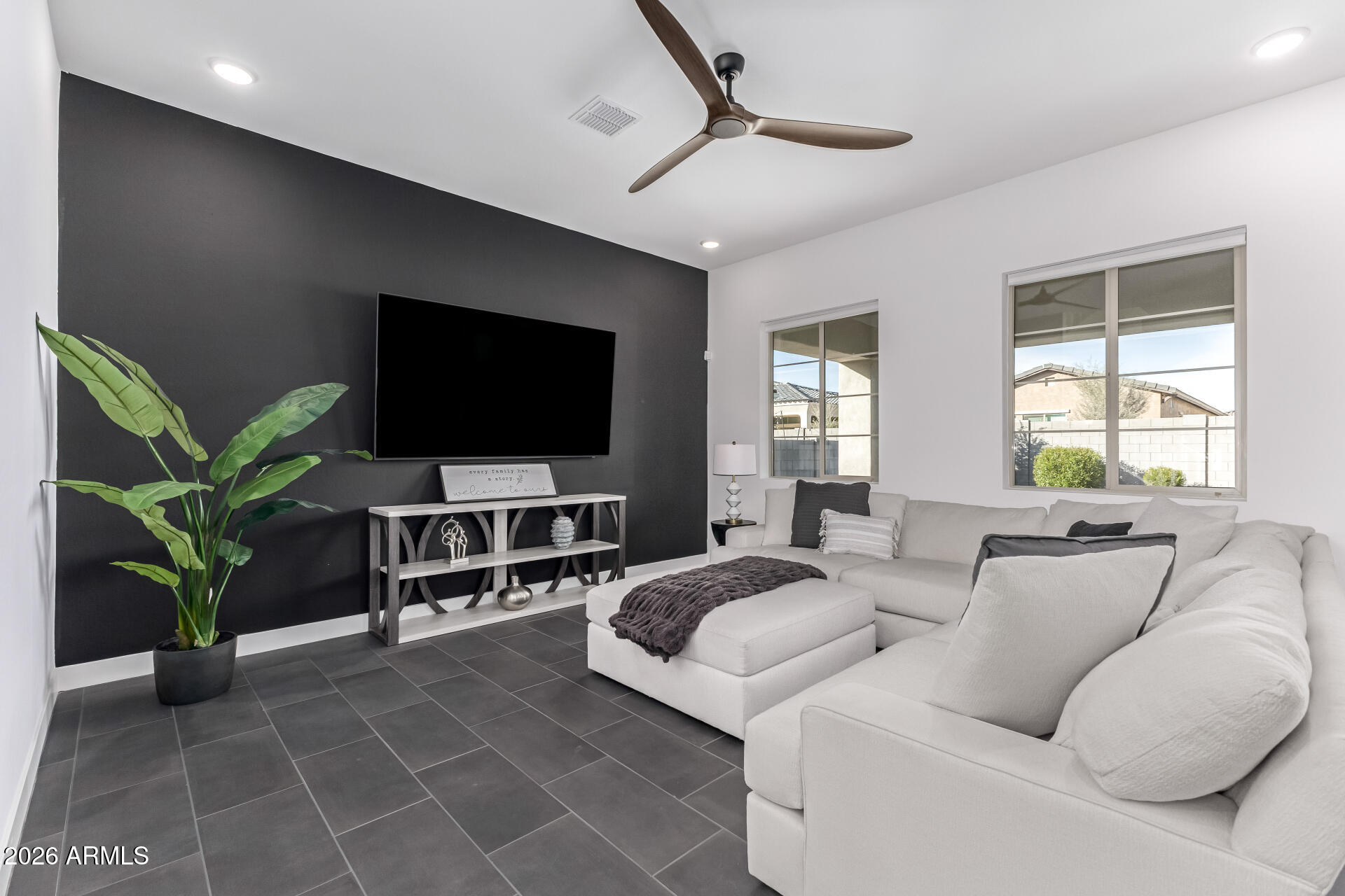 Living room with a white sectional, charcoal TV wall, dark tile flooring, and two sunlit windows.