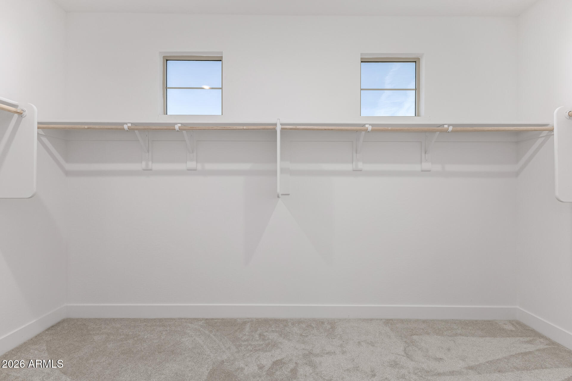 Empty walk-in closet with two high windows and a long wooden clothes rail.