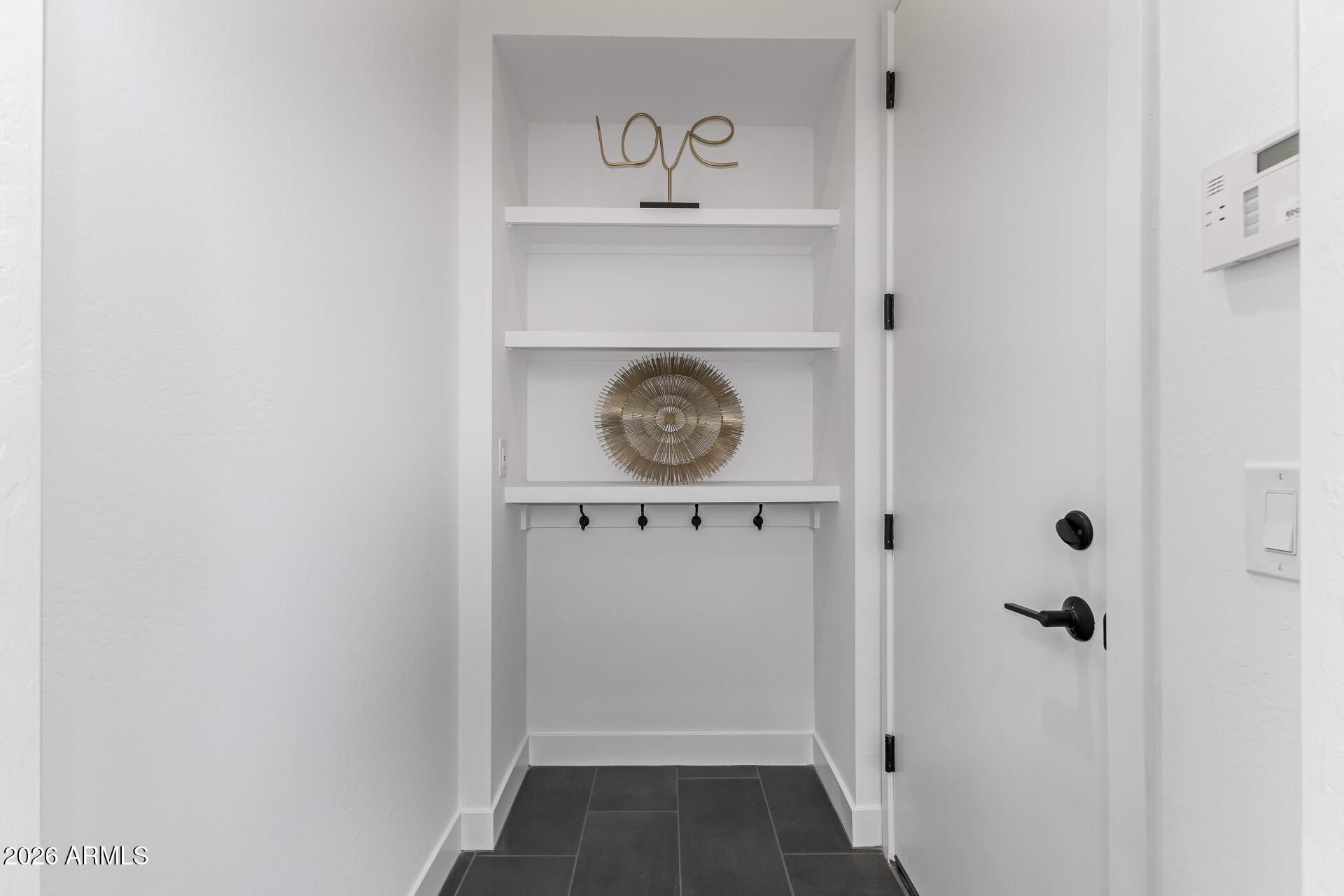 Entryway with built-in display shelves and hooks beside a white door.
