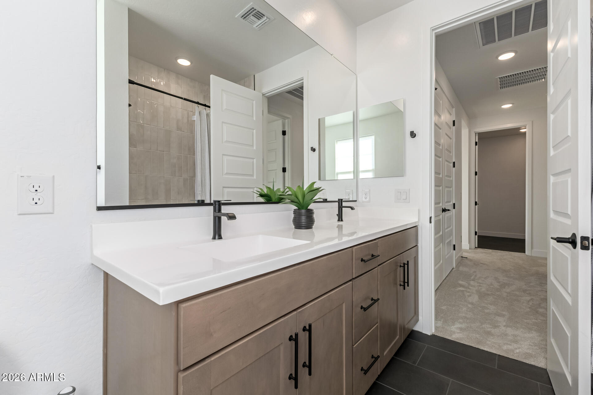 Bathroom with a taupe double vanity, white countertop, black faucets, and large mirrors.