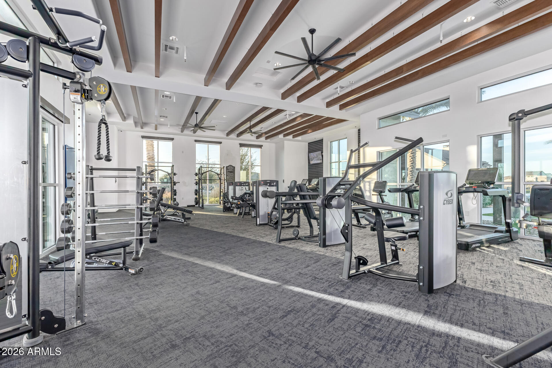 Fitness center with weight machines and treadmills beneath exposed wood ceiling beams.