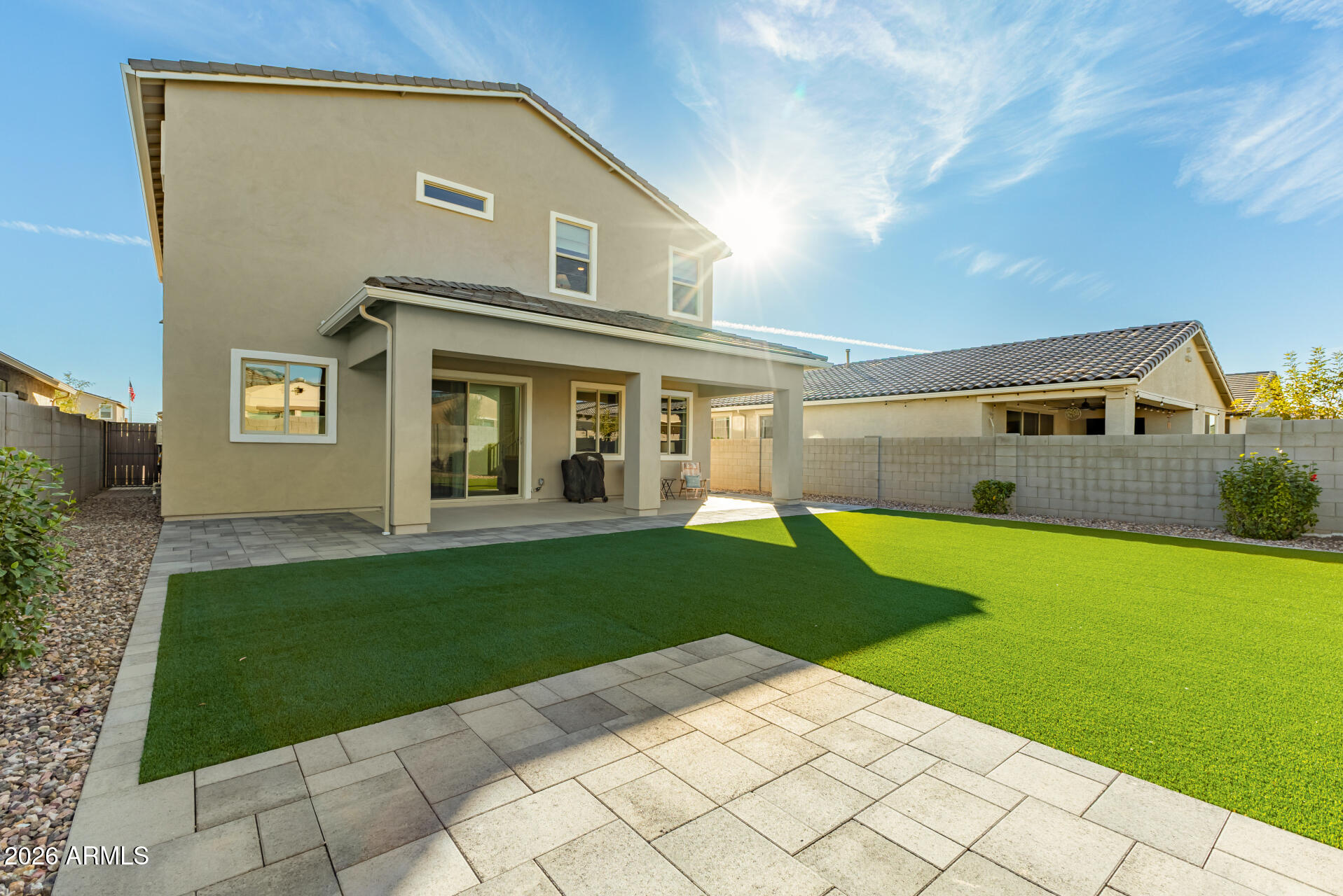 Two-story home with a covered patio, artificial turf lawn, and broad paver patio.
